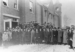 A large collection of citizens outside the city building/fire station on a cold winter day. 