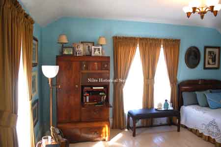 View of bedroom showing wooden wardrobe, sitting bench and typical lighting fixtures.